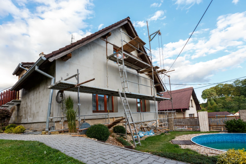 A two-story house under renovation with scaffolding , installing windows and balcony.